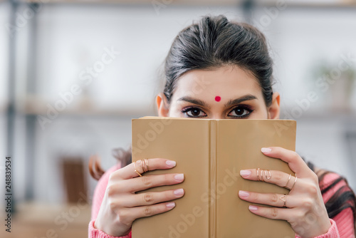 indian student with bindi holding book in front of the face photo