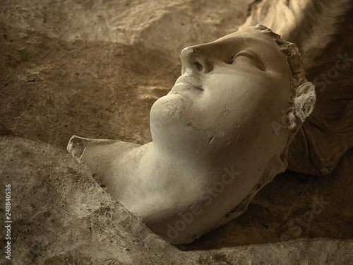 A broken statue head laying on the ground in Rome