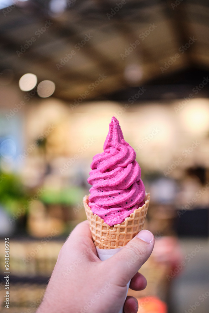 Dragonfruit ice cream in a waffle cone held in a mans hand