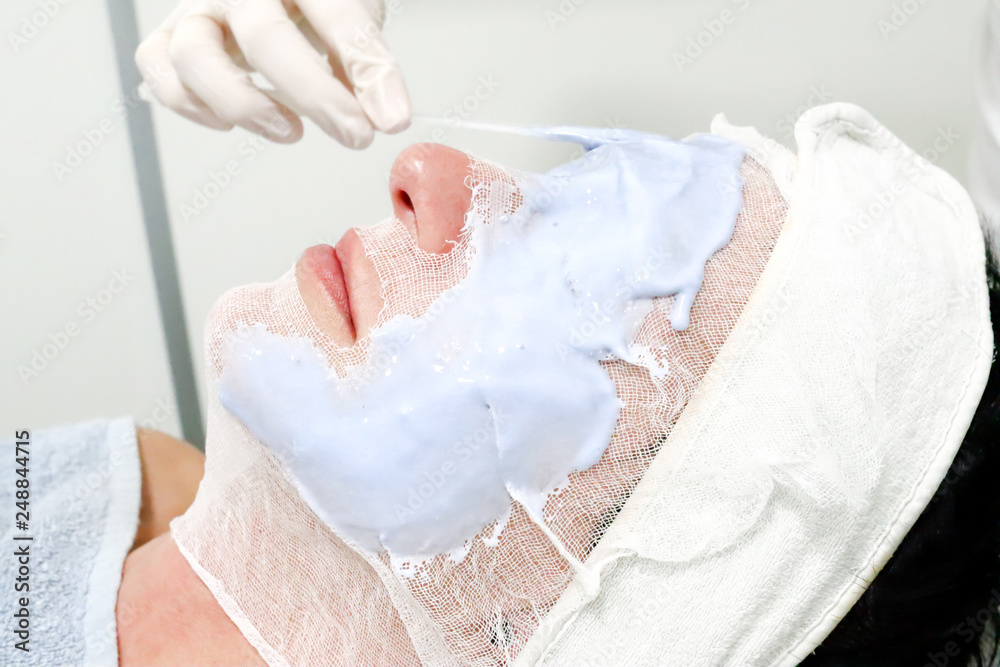 beautician worker applying  cosmetic Caviar peel off mask for facial skin care  to female client in beauty salon 