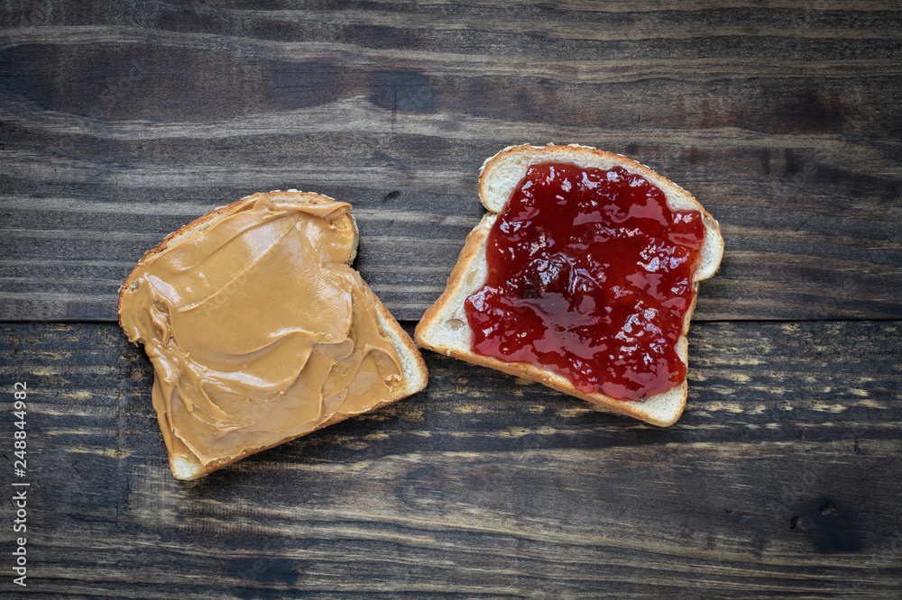 Fototapeta premium Top view of open face homemade peanut butter and strawberry Jelly sandwich on oat bread, over a rustic wooden background.