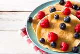 Pancakes with raspberries, blueberries and honey on white wooden table. Close up