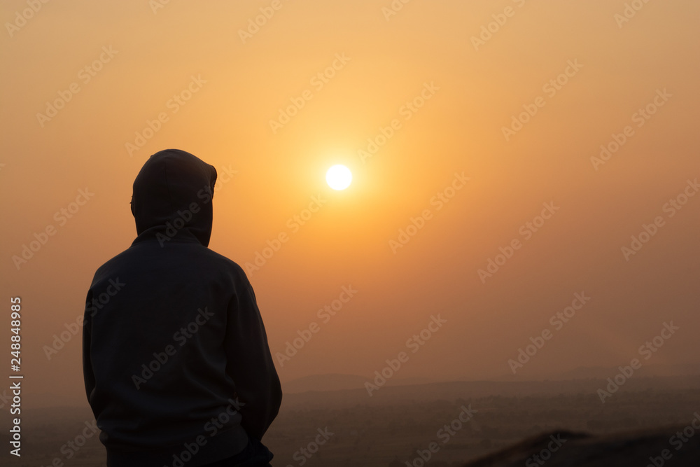 A person weareed hoody sat on the mountain by watching sunset.