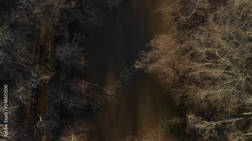 Flying over and looking down into the muddy Appomattox River that flows under High Bridge Trail in Virginia. The setting sun casts deep shadows over the riverbank. UHD aerial footage. photo