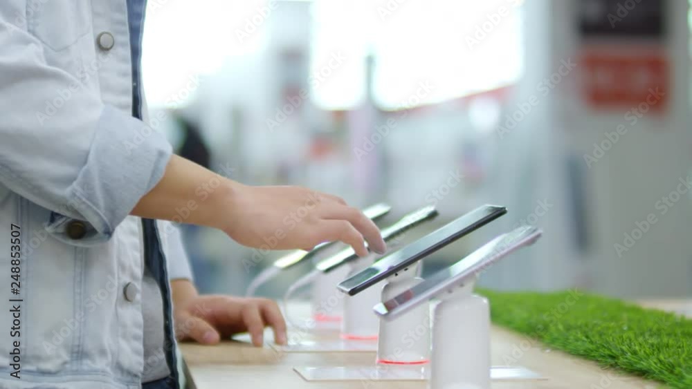 Close up hand of unrecognizable young man using touchscreen of smartphone when choosing between different models in gadget store Close up hand of unrecognizable young man using touchscreen of smartphone when choosing between different models in gadget store