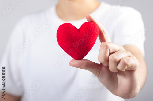 Woman s hand with white t-shirt holding red fabric heart shaped