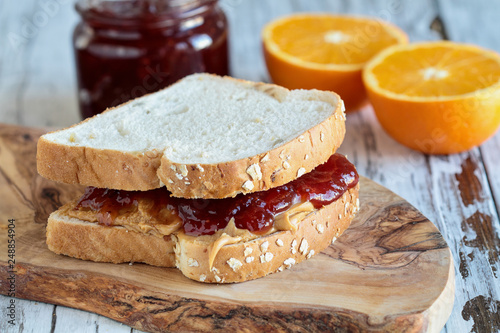 Homemade Peanut Butter and Jelly Sandwich on oat bread, over a rustic wooden background with fruit in the background ready for lunch. photo