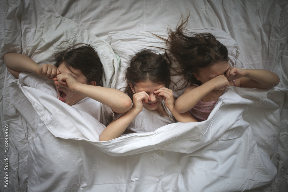 three children rub eyes, lying under blanket three children rub eyes, lying under blanket