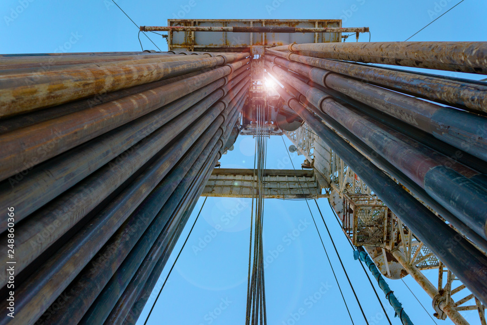 Fototapeta premium Oil and Gas Drilling Rig onshore dessert with dramatic cloudscape. Oil drilling rig operation on the oil platform in oil and gas industry. Land drilling rig blue sky