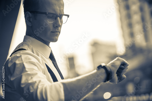 smart caucasian businessman white shirt and red tie hand up check time schedule with sunset building background