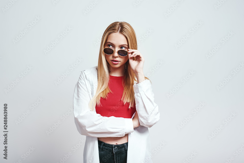 Fashion girl. Close up portrait of attractive blonde woman adjusting her sunglasses and looking at camera. Beauty concept