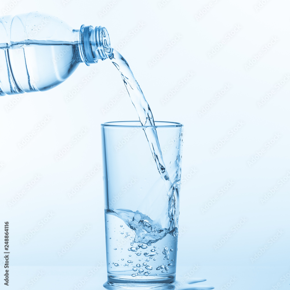 Pouring water from bottle into glass on blue background.