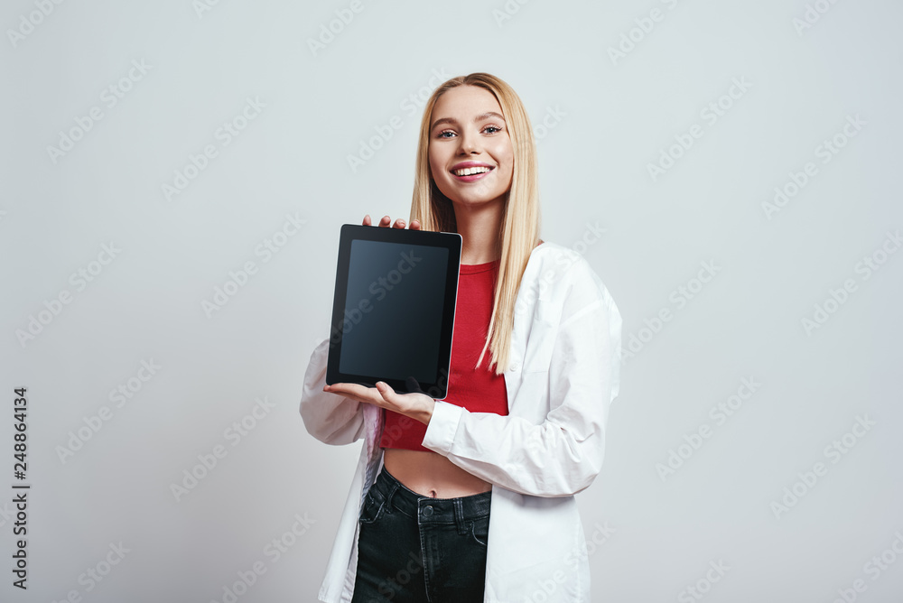 Look over here! Excited young blonde woman holding and showing the screen of her modern touchpad. Digital concept Look over here! Excited young blonde woman holding and showing the screen of her modern touchpad. Digital concept
