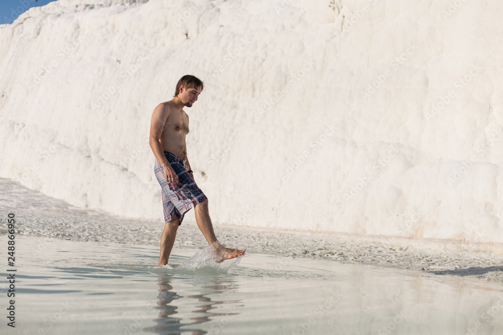 Natural travertine pools and terraces in Pamukkale. Cotton castle in southwestern Turkey. Young man walking at the pool in natural bath. Beautiful man looks Pamukkale (Cotton Castle)