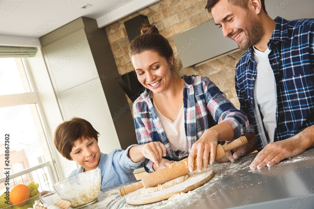 Family at home standing at table in kitchen rolling dough with pin together joyful Family at home standing at table in kitchen rolling dough with pin together joyful