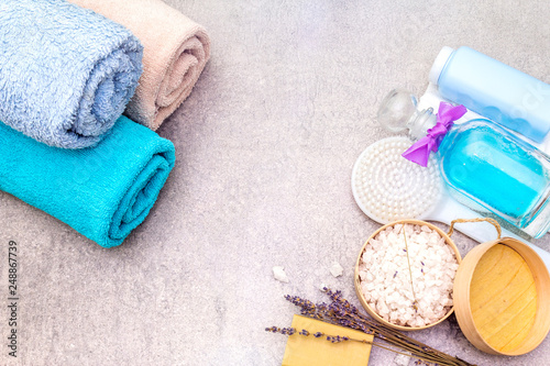Spa concept, natural ingredients. Bath towels, sea salt with lavender, natural olive soap, shower gel, brush. On a stone background, top view