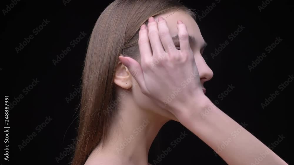 Portrait in profile of young and slim caucasian girl with nude make-up tenderly touching her face on black background. Portrait in profile of young and slim caucasian girl with nude make-up tenderly touching her face on black background.