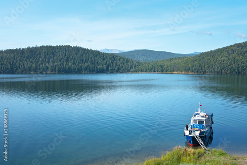 Lake Baikal in summer. The picturesque cove in Chivyrkuy Bay. Tourist catches fish from the board of the pleasure craft. On the opposite shore of the bay tourist camp