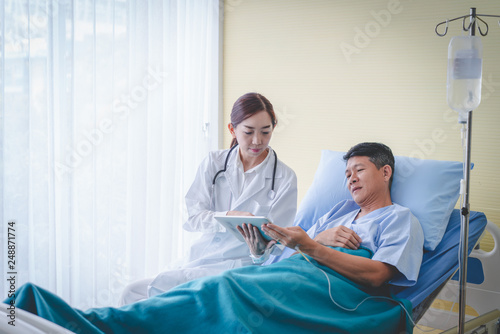Asian female doctor with male patient is checking the results from the tablet.