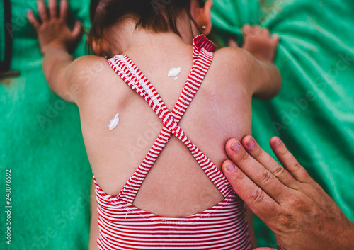 Niña echándose crema mientras toma el sol en la playa