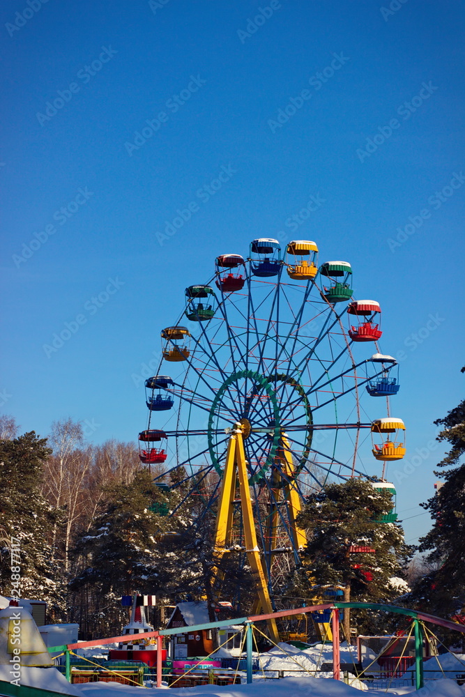 Old abandoned rusty ferris wheel in winter in a park with deep blue sky in the background