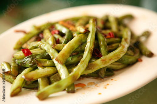A traditional Chinese dish of green string beans with red chili pepper, served in a white plate. Beijing, China.