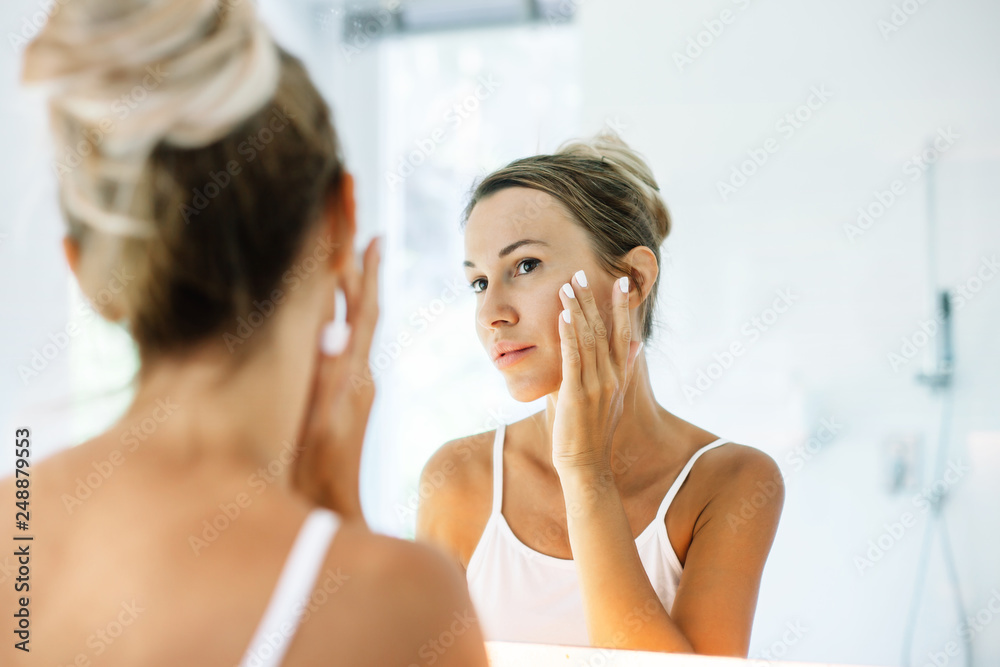 Woman applying face cream in bathroom Woman applying face cream in bathroom