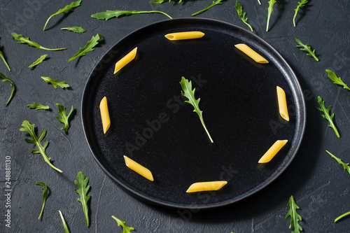 The concept of pasta Penne with arugula, minimalism. Dark background, side view