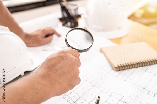 architect or civil engineer checking or inspected builing plan with magnifier in office.