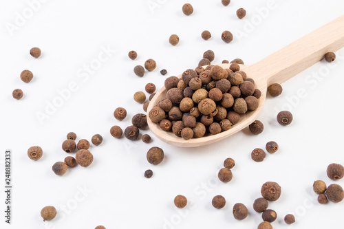 Allspices or Jamaica pepper in wooden spoon isolated on white background. Closeup.