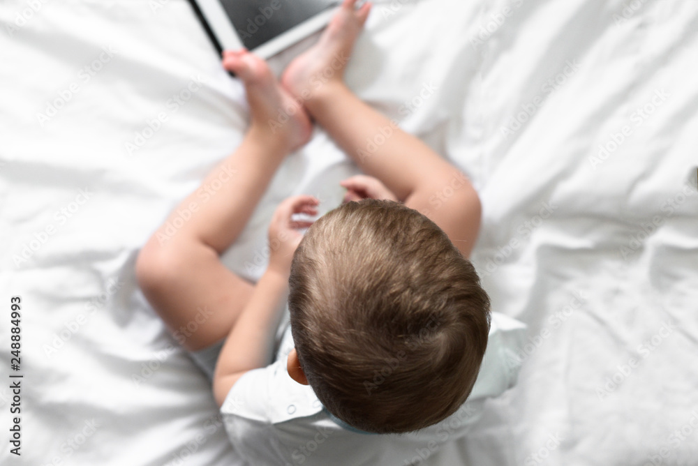 boy on a bed with white linens playing in the tablet boy on a bed with white linens playing in the tablet