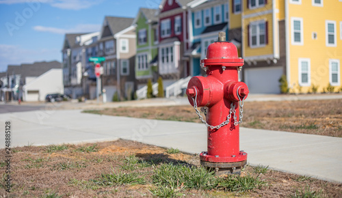 Fototapeta Naklejka Na Ścianę i Meble -  Close up bokeh shot of a bright red fire hydrant with brightly colored townhouses in the background.