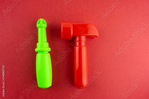 Toy red hammer and green screwdriver on a red paper background.