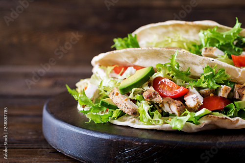 Pita bread sandwiches with grilled chicken meat, avocado, tomato, cucumber and lettuce served on wooden background. Close up. Healthy fast food concept.