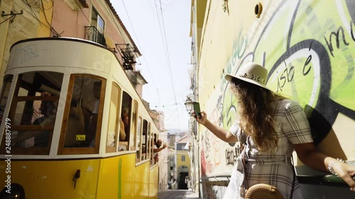 Side view of young tourist with smartphone taking selfie near retro tram on rails in Lisbon