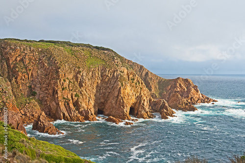 Illuminated by the evening sun, surf swirls around the bottom of sheer cliffs and into sea caves on Cape Woolamai, Phillip Island, Victoria, Australia.