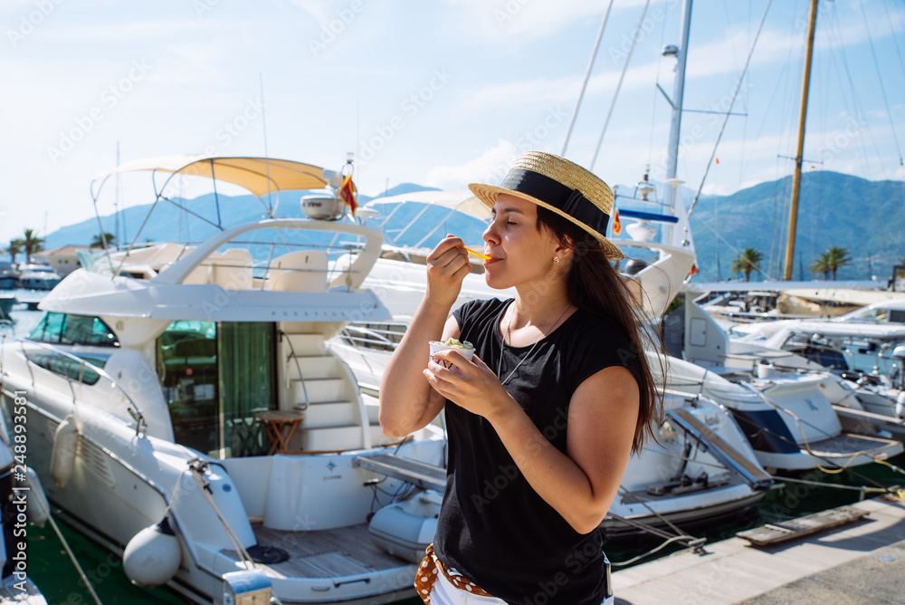 young pretty woman eating ice cream at hot summer day. yachts on background