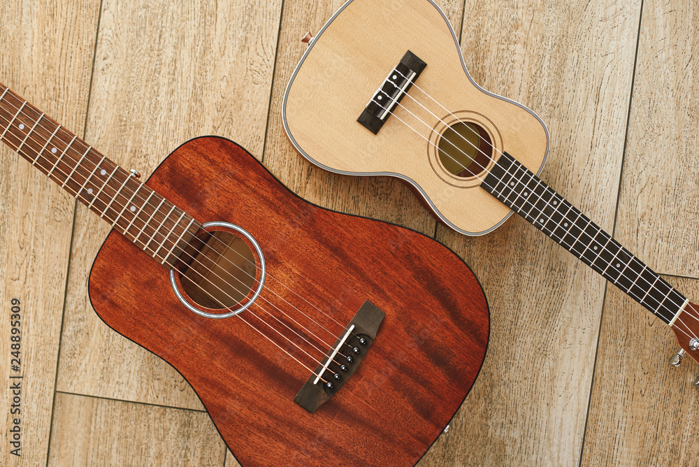Perfect sound. Top view of the acoustic and ukulele guitars lying close to each other on the wooden floor. Music concept Perfect sound. Top view of the acoustic and ukulele guitars lying close to each other on the wooden floor. Music concept