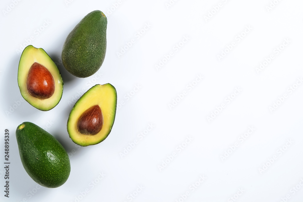 Minimal composition with whole and halved nutrient dense avocado fruit slices full of heart healthy monounsaturated fat on gray glass table top. Close up, copy space, top view, background. Minimal composition with whole and halved nutrient dense avocado fruit slices full of heart healthy monounsaturated fat on gray glass table top. Close up, copy space, top view, background.