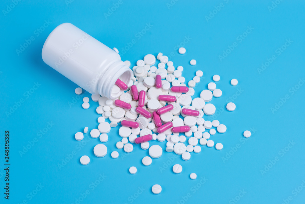 White and pink pills, tablets and white bottle on blue background.