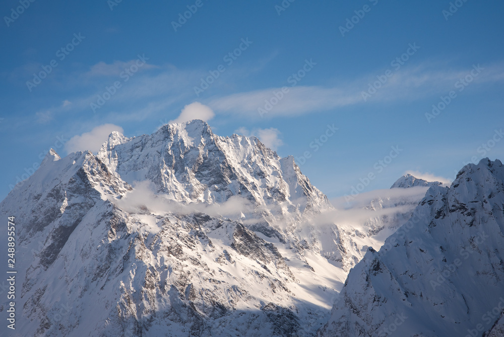mountain peaks of Dombai mountains covered with snow surrounded by thick clouds against the blue sky. February 2019