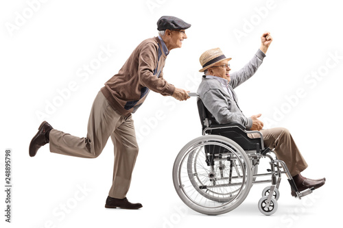 Elderly man riding a longboard and pushing a man in a wheelchair