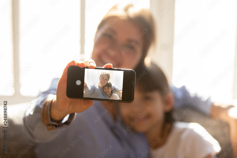 Happy mother embracing child daughter holding phone taking selfie