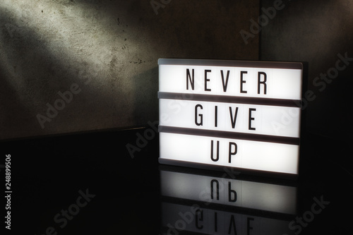 Never give up motivational message on a light box in a cinematic moody background