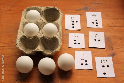 Clever way to teach a visually impaired child to read braille with table tennis balls in an egg container with alphabet cards with raised braille dots nearby.