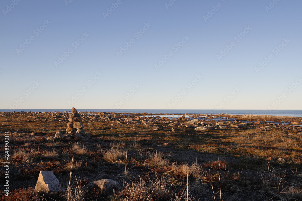 Inukshuk or Inuksuk on a rocky tundra with water in the background in late June in the arctic community of Arviat, Nunavut, Canada