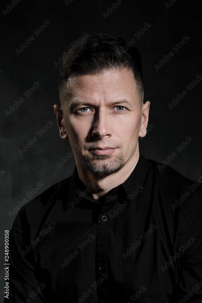 Portrait of a handsome man 40 years old on a dark artistic background close-up. Brunette, with gray hair, black beard and black shirt.