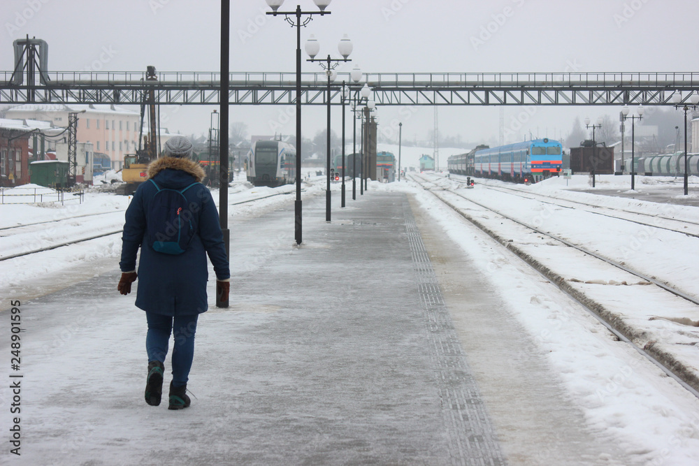 person walking on empty railway platform, frozen platform in the bitter cold in the winter. asphalt in the ice, waiting for the arrival of the train. meet tourists or travelers. person walking on empty railway platform, frozen platform in the bitter cold in the winter. asphalt in the ice, waiting for the arrival of the train. meet tourists or travelers.
