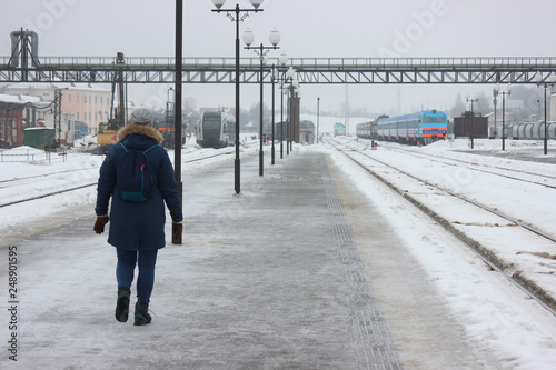 person walking on empty railway platform, frozen platform in the bitter cold in the winter. asphalt in the ice, waiting for the arrival of the train. meet tourists or travelers.