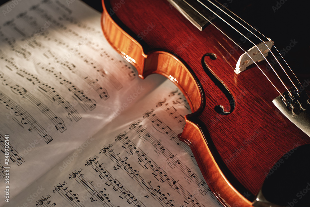 Fototapeta premium How to Read Violin Notes? Close up view of brown wood violin lying on the sheet with music notes.